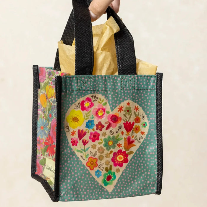 A hand holds a small bag featuring a colorful floral design against a neutral background.