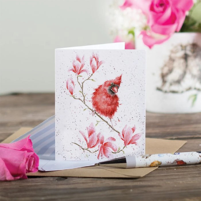 A vibrant red cardinal sitting on a branch, illustrated on a greeting card.
