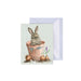 A decorative card displaying a bunny nestled in a pot with vibrant flowers around it.