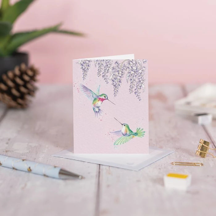 A vibrant pink card showcasing a hummingbird, elegantly hovering with its wings spread wide.