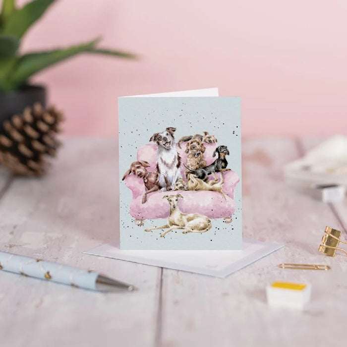 A whimsical greeting card showing dogs comfortably seated on a pink couch, perfect for dog lovers.