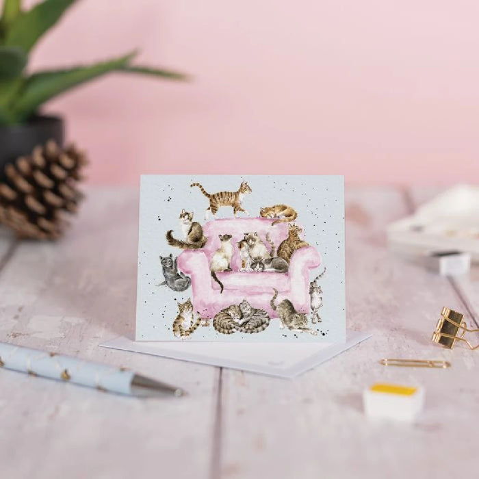 A pink sofa adorned with playful cats, featured on a cheerful greeting card design.