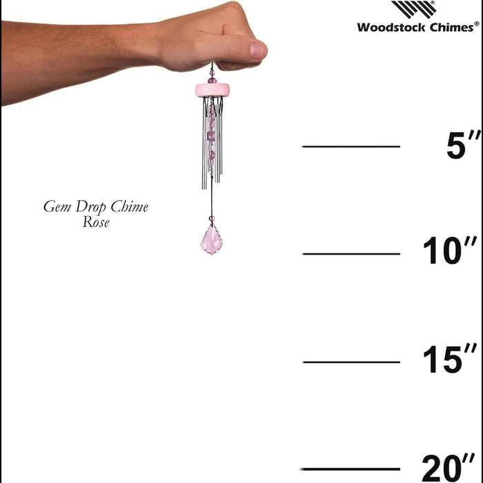 Hand holding a pink wind chime with measurement scale on a white background