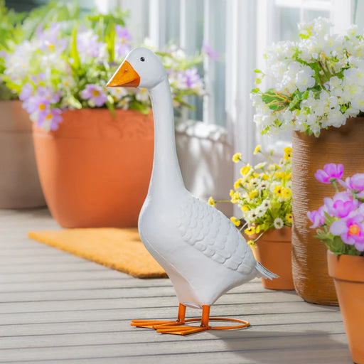  A white goose statue stands on a porch surrounded by colorful flowers.