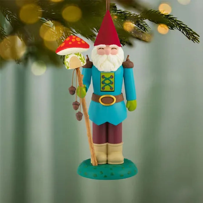 Colorful gnome ornament with a mushroom and staff hanging from a tree.