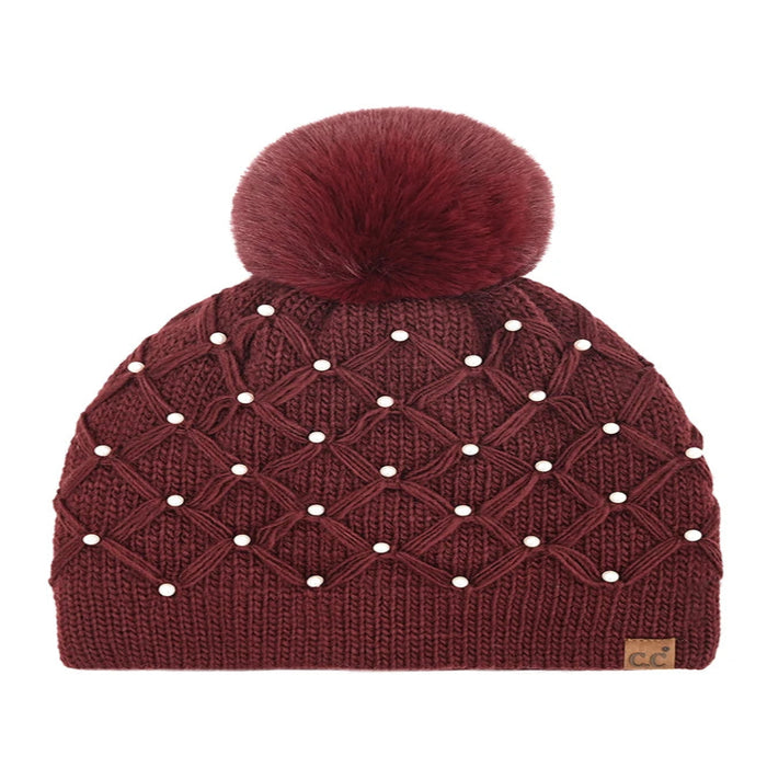 burgundyCheveux Corp beanie with a raised diamond crochet pattern, pearl accents, ribbed cuff, large fluffy ivory pom, and small brown logo patch.