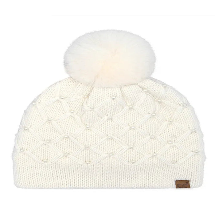 Ivory Cheveux Corp beanie with a raised diamond crochet pattern, pearl accents, ribbed cuff, large fluffy ivory pom, and small brown logo patch.