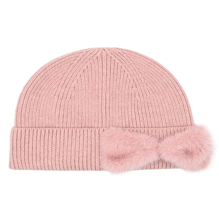 Cheveux Corp blush pink ribbed knit beanie with a rounded crown, wide folded cuff, and large matching faux fur bow on the right side of the cuff, shown against a white background.