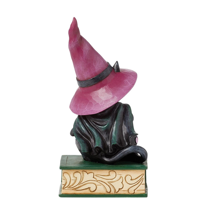 Back view of black cat figurine with flowing green cape and tall pink witch hat sitting on a decorative spellbook.