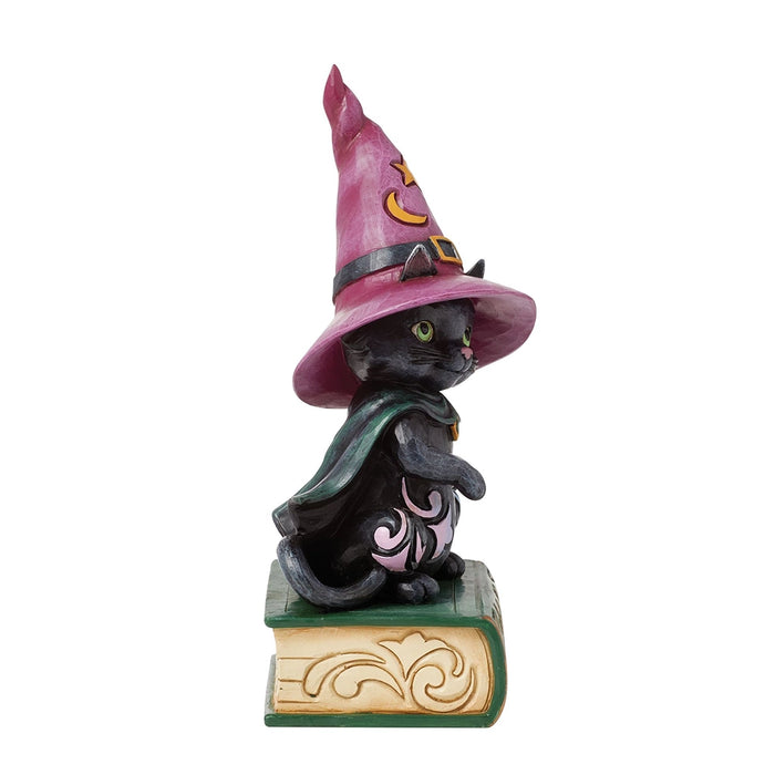 Side view of black cat figurine in witch costume, showing pointed pink hat, cape, and spellbook base.