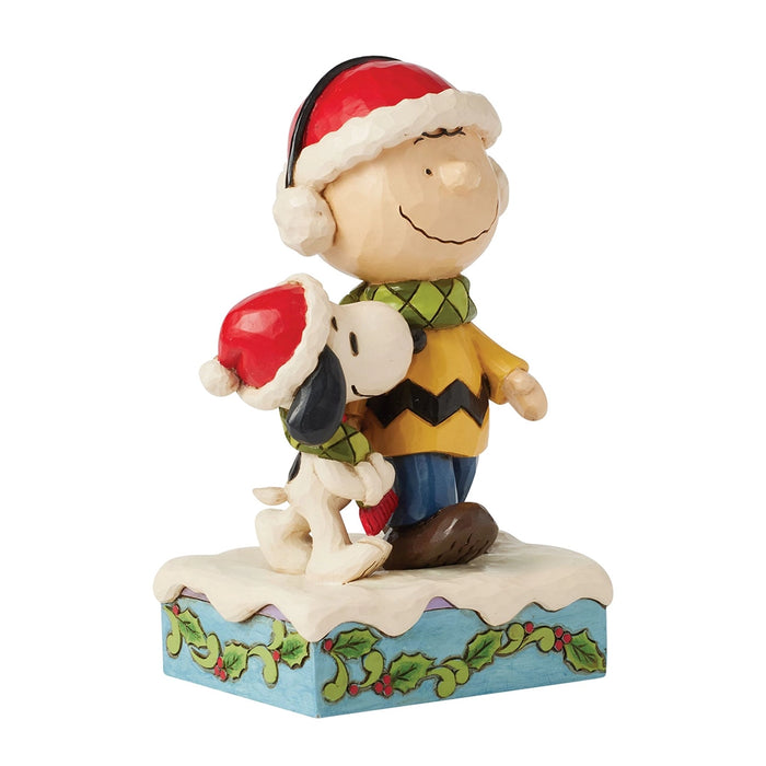 Jim Shore Charlie Brown and Snoopy figurine wearing scarves and Santa hats on snowy base.