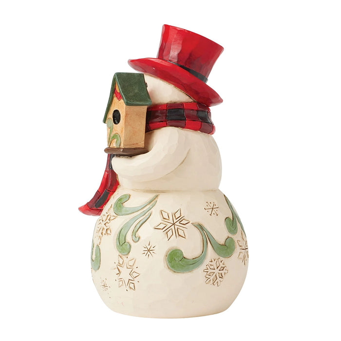 Side view of hand-carved Jim Shore snowman with birdhouse and plaid scarf.
