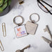 A square keychain displaying an artistic depiction of a bird among floral elements.