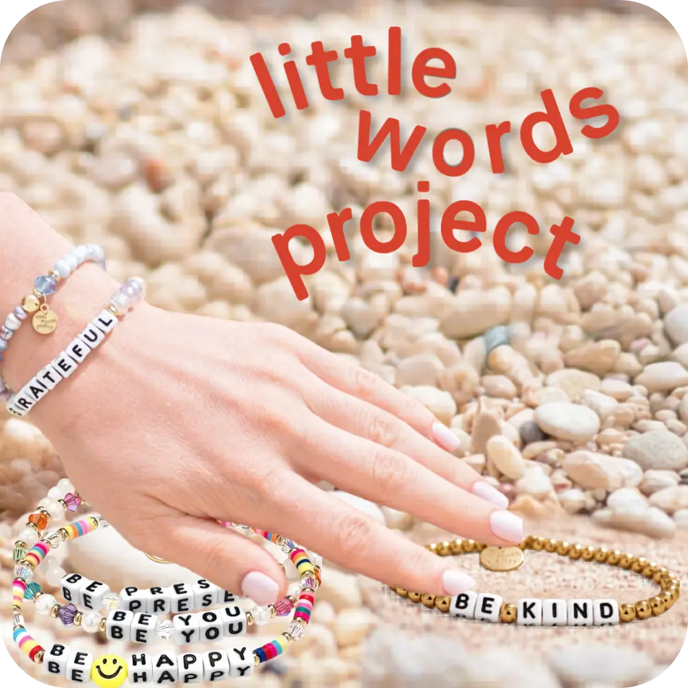 Hand wearing multiple bracelets with inspirational messages on pebbles, featuring 'little words project' text.