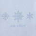 Close-up of Life Is Good Doodle Snowflakes graphic featuring three hand-drawn snowflakes and logo on soft blue fabric.