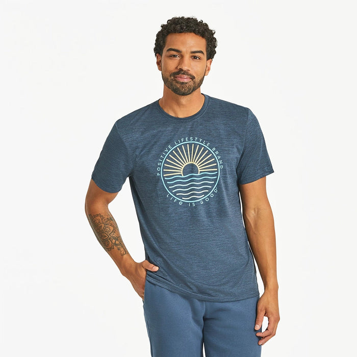 Front view of Life Is Good Men's Sun & Waves Crusher Tee on model – navy blue graphic t-shirt with sunrise and wave design, paired with blue shorts.