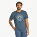 Front view of Life Is Good Men's Sun & Waves Crusher Tee on model – navy blue graphic t-shirt with sunrise and wave design, paired with blue shorts.