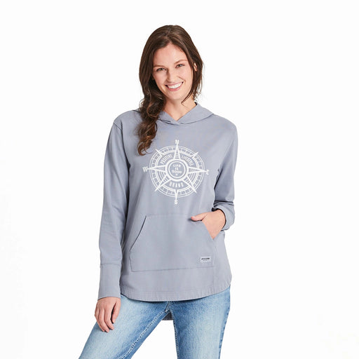 Woman wearing a light blue-gray Life is Good hoodie featuring a white compass design and "Positive Lifestyle Brand" text, hands in kangaroo pocket.