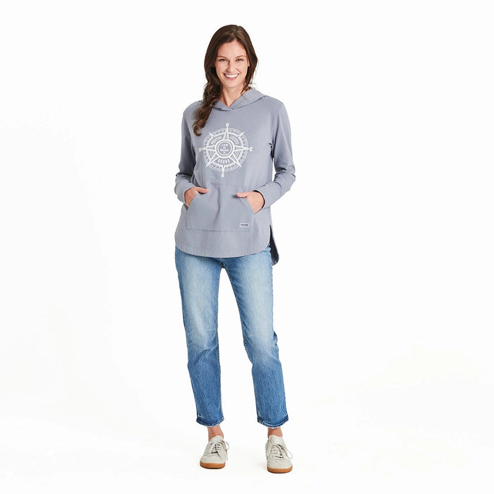 Full-length view of a smiling woman wearing the Life is Good compass hoodie with light blue jeans and casual sneakers, standing hands-in-pocket.