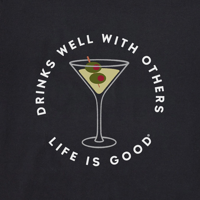 Close-up of Life Is Good Women's Martini Tee graphic – illustrated martini glass with green olives and slogan “Drinks Well With Others” above “Life Is Good” in white font on black fabric.