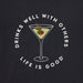 Close-up of Life Is Good Women's Martini Tee graphic – illustrated martini glass with green olives and slogan “Drinks Well With Others” above “Life Is Good” in white font on black fabric.