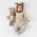 Baby wearing a knitted deer hat and overalls, holding a Little Cuddle + Kind Elliott the Fawn
