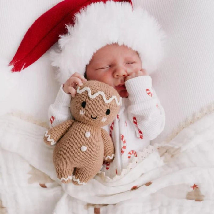 Sleeping baby in Christmas pajamas cuddling Cuddle + Kind Baby Gingerbread Doll – White Icing.