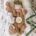 Baby dressed in cozy knit outfit lying with Cuddle + Kind baby snowman, gingerbread doll, and gingerbread house plush, holding a “My First Christmas” sign.