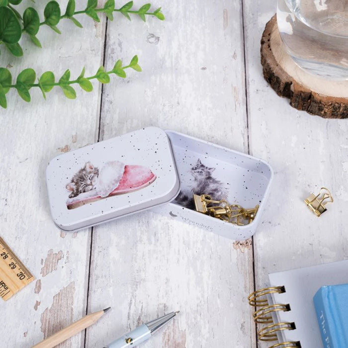 A cozy scene of a cat curled up and sleeping in a tin box, creating a charming and serene atmosphere.