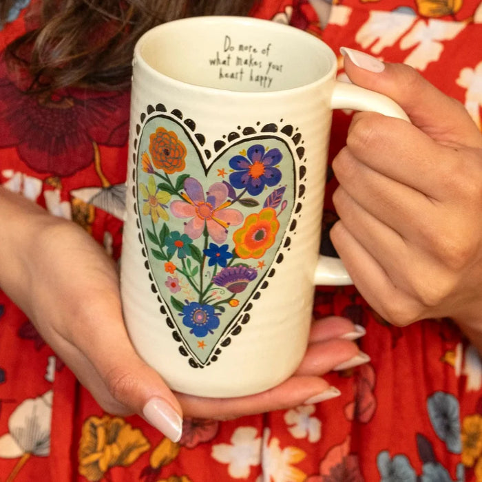 A woman with a warm smile holds a floral heart-shaped mug, showcasing a cozy and inviting atmosphere.