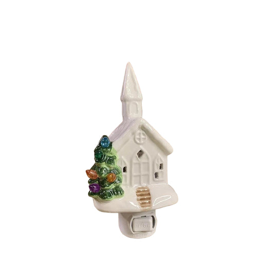 Decorative night light shaped like a small church with a Christmas tree in front of a brick wall.