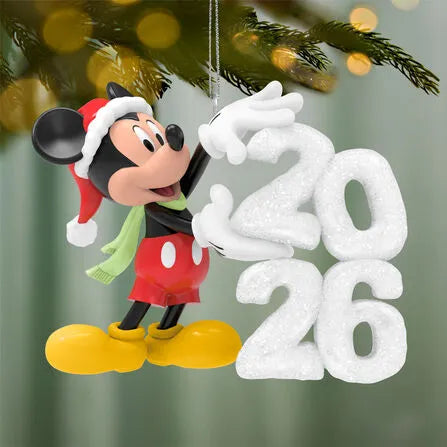 Disney Mickey Mouse 2026 Christmas tree ornament hanging on pine branch with warm holiday lights