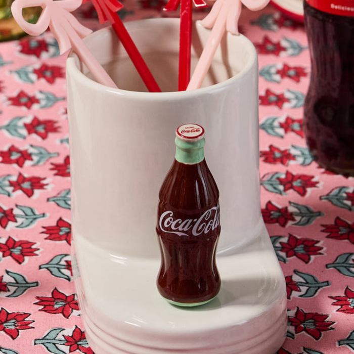 Nora Fleming Coke® Bottle Mini in ceramic inserted in serving base with bow drink stirrers and Coca-Cola décor