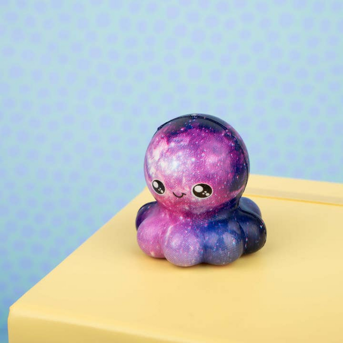 Cute, colorful octopus-shaped toy with a galaxy design on a yellow surface against a light blue background.