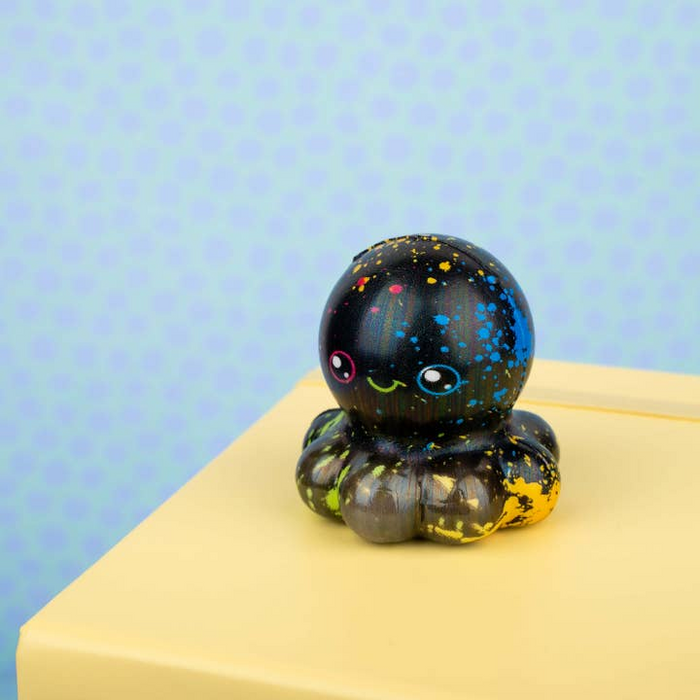 Decorative glass octopus with black speckled ball on a yellow surface against a blue polka dot background