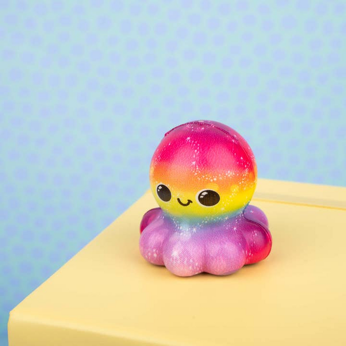 Colorful octopus-shaped toy with a rainbow pattern on a yellow surface against a light blue background