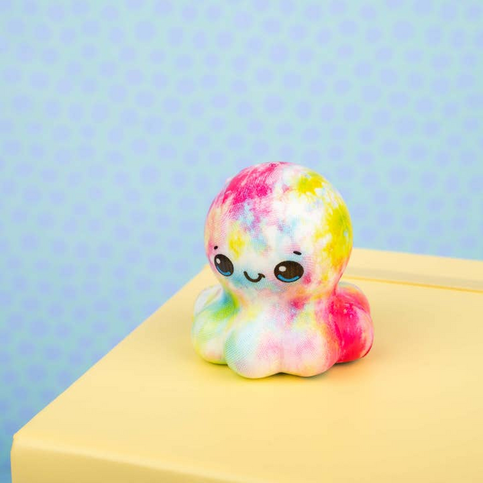 Colorful tie-dye plush toy on a yellow surface with a light blue background
