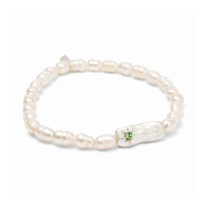 A delicate bracelet adorned with pearls, representing good fortune, resting on a textured surface.