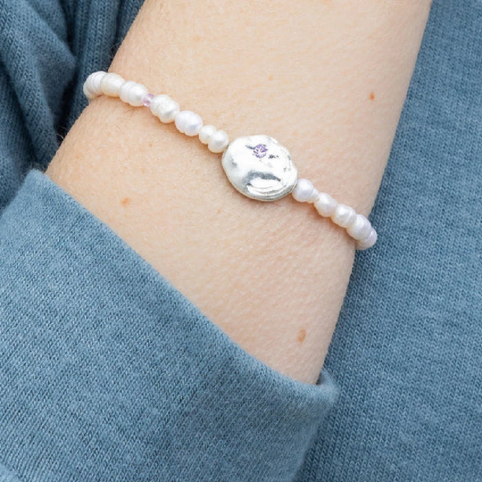 White pearl bracelet with a striking purple stone centerpiece.
