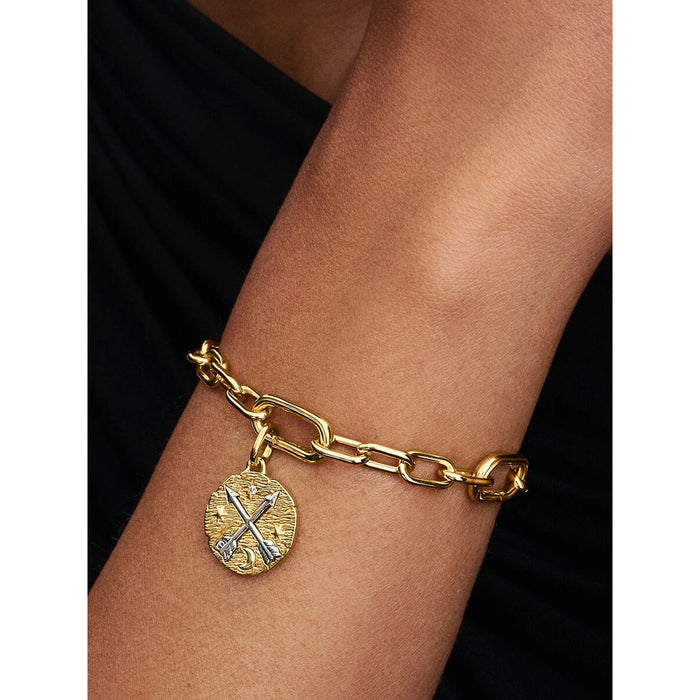 Close-up of a gold chain bracelet on a wrist, featuring the Pandora Crossing Arrows Medallion Charm with engraved arrows, stars, and a crescent moon.