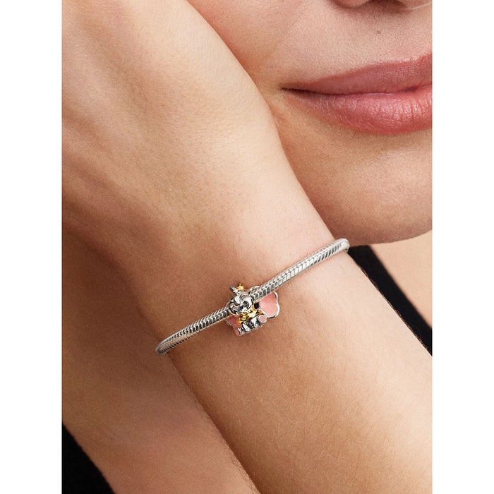 Close-up of a silver bracelet featuring a Disney Dumbo charm with pink enamel ears, a yellow ruffle collar, and a glittery hat.
