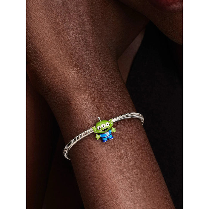 Close-up of a Pandora Disney Pixar Toy Story Alien Charm in sterling silver with green and blue enamel, styled on a Pandora Moments bracelet on a wrist.