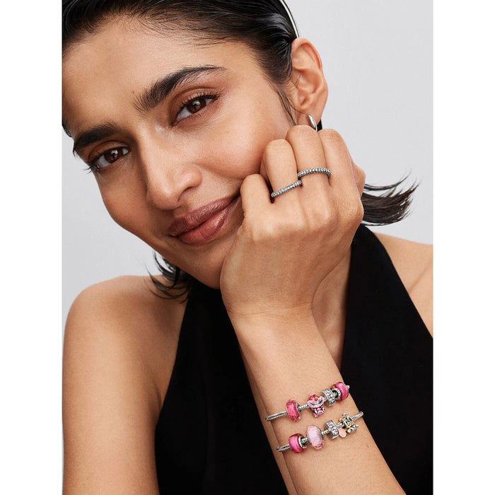 Woman wearing stacked silver charm bracelets, including the Disney Dumbo charm paired with pink enamel and Murano glass charms.