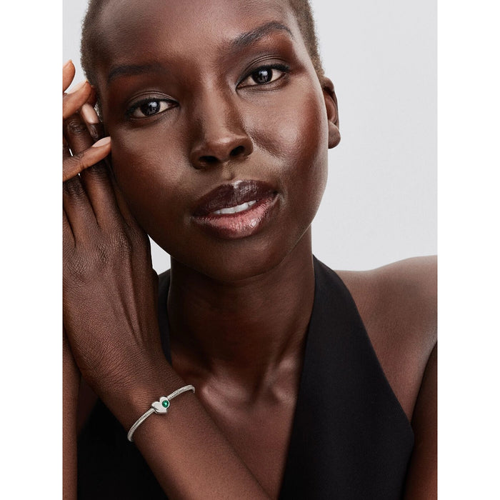 A woman wearing a silver Pandora bracelet with a green stone heart charm, styled with a sleeveless black top.