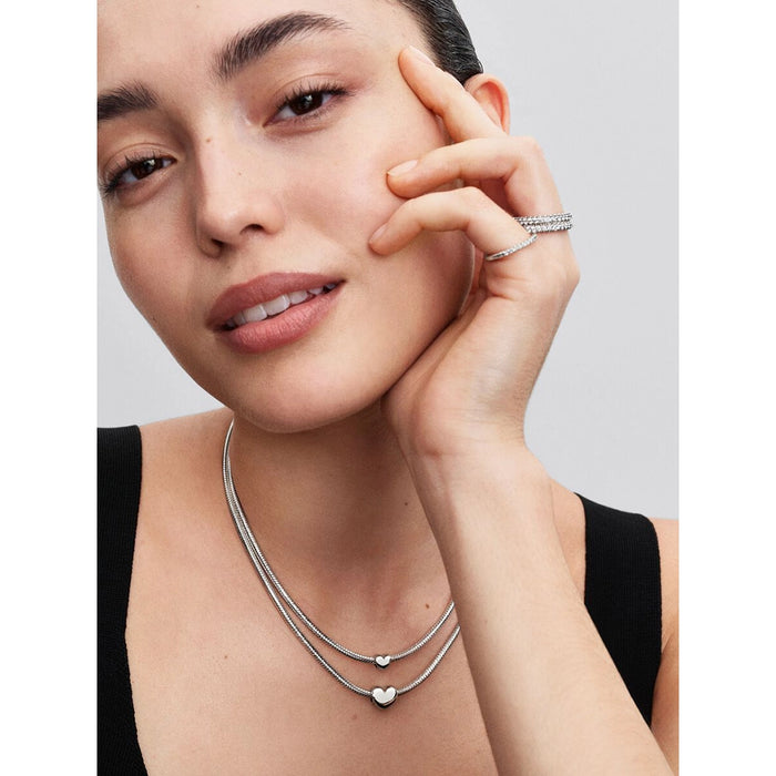 Close-up of a woman wearing two layered Pandora necklaces, each styled with a polished silver heart mini charm.