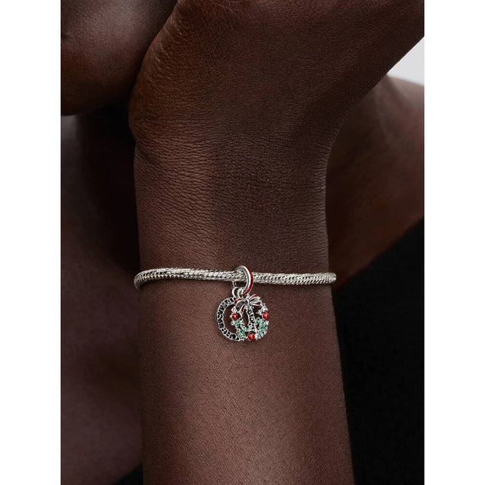 Pandora Holiday Wreath Double Dangle Charm worn on a model’s wrist, showing festive wreath details with red and green accents.