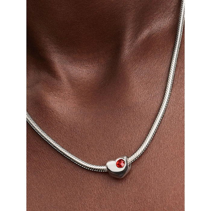 Silver necklace with a heart-shaped pendant featuring a red gemstone on models neck.