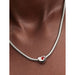Silver necklace with a heart-shaped pendant featuring a red gemstone on models neck.