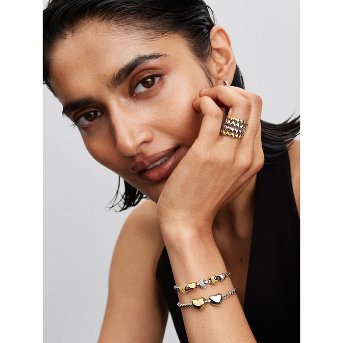 Woman wearing Pandora silver woven bracelet stacked with gold and silver charms and rings.