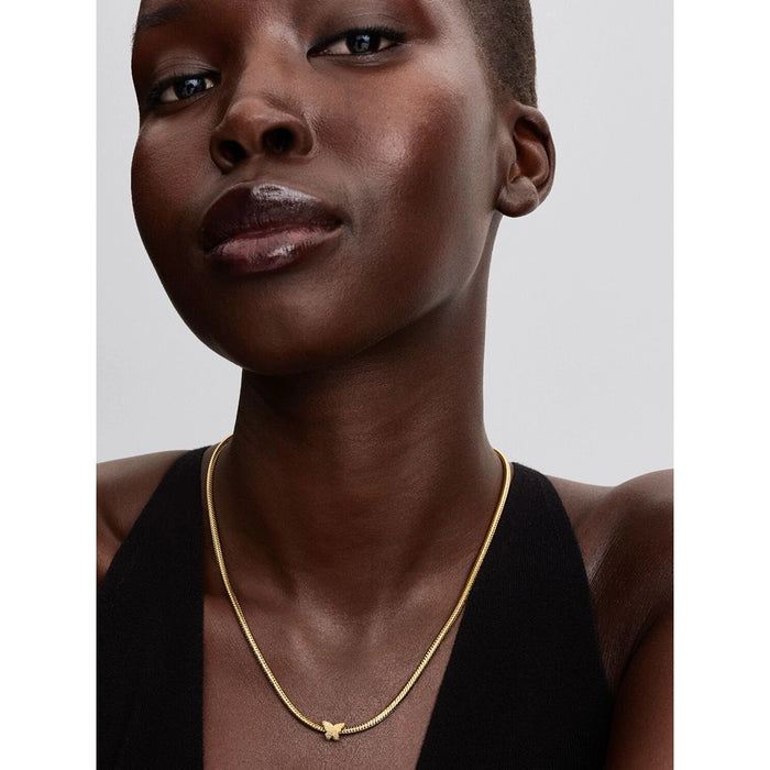 Model close-up wearing a gold necklace with a textured butterfly-shaped charm centered on a snake chain.